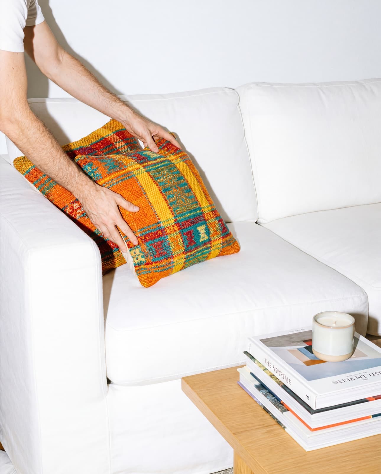 Hands styling a cushion on a sofa — the Kept touch